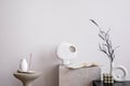 Aesthetic interior of living room with white wall, marble stand, round coffee table, vase with dried flowers, green candle and