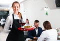 Affable female waiter is standing with order in luxury restaurante
