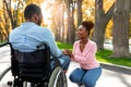 Affectionate black woman holding her paraplegic husband's hand, expressing love at autumn park