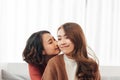Affectionate girl kissing her happy sister or friend in the living room at home with a homey background