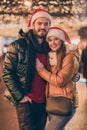 Affectionate jolly couple hugging on x-mas fair under evening outside tradition lights wear winter coats santa claus