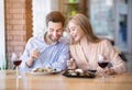 Affectionate millennial couple eating salad and drinking wine on romantic dinner at cafe, celebrating Valentine`s Day