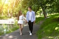 Affectionate millennial couple holding hands and walking along pathway in summer park