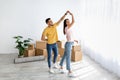 Affectionate multiracial couple dancing in their house among carton boxes on moving day, free space