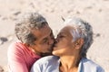 Affectionate multiracial senior couple kissing on lips while enjoying sunny day at beach