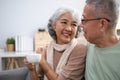 Affectionate senior Asian couple sharing warm embrace on the sofa, celebrating their enduring love and togetherness. Elderly