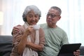 Affectionate senior Asian couple sharing warm embrace on the sofa, celebrating their enduring love and togetherness. Elderly