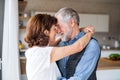 Affectionate senior couple in love standing indoors at home, hugging.