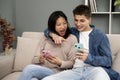 Affectionate young couple with mobile phones relaxing on sofa. Happy diverse woman and man hugging using smartphone Royalty Free Stock Photo