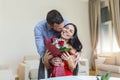 Affectionate young man giving his beautiful young wife a bouquet of red roses and kissing her on Valentines day , romantic happy Royalty Free Stock Photo