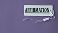 AFFIRMATION - word on white paper with thread on a purple background