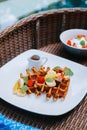 Waffles in a plate with indonesian fruit salad and a cup of brown sugar sauce