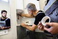 Affordable repairing. Aged plumber, repairman in uniform fixing electric boiler with wrench while his young colleague