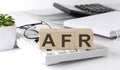 AFR written on a wooden cube on keyboard with office tools