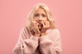 Afraid young lady biting nails with worry, having emotional stress, reacting to scary news, pink studio background