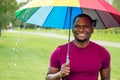 African america man standing under colorful umbrella in summer park checking for rain