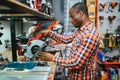 African americam man buying modern electric drill while standing in tool. Hardware construction site objects concept Royalty Free Stock Photo
