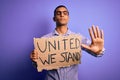 African american activist man asking for union holding banner with united stand message with open hand doing stop sign with