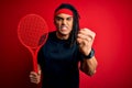 African american afro sportsman with dreadlocks holding tennis racket over red background annoyed and frustrated shouting with