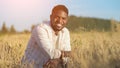 African American agriculturist sits on wheat field smiling