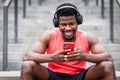 African american athletic guy listens to music in wireless headphones and smiles outdoors, a man sits on the steps and looks into Royalty Free Stock Photo