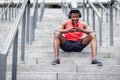 African american athletic guy listens to music in wireless headphones and smiles outdoors, a man sits on the steps and looks into Royalty Free Stock Photo