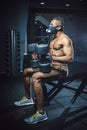 African american athletic man in mask sitting and waiting and looking at himself before lifting dumbbells in front of the mirror. Royalty Free Stock Photo