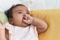 African american baby sitting on bed sucking hand at bedroom Royalty Free Stock Photo