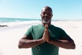 African american bald senior man with eyes closed meditating in prayer position at beach, copy space Royalty Free Stock Photo