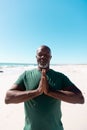 African american bald senior man with eyes closed meditating in prayer position at beach, copy space Royalty Free Stock Photo