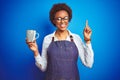 African american barista woman wearing bartender uniform holding cup over blue background surprised with an idea or question