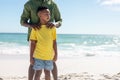 African american boy looking away while standing ahead of father at beach against sky Royalty Free Stock Photo