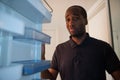 An African American boy opens the fridge and realizes it is empty. He has a sad and worried facial expression. Crisis and poverty Royalty Free Stock Photo
