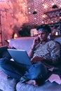 African American boy sitting barefoot on the couch and checking his mail while talking on the phone. Royalty Free Stock Photo