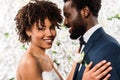 African american bride hugging handsome bridegroom near flowers