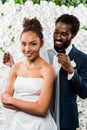 African american bridegroom touching white veil and smiling near bride and flowers Royalty Free Stock Photo