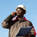 African american builder with work papers talks on smartphone