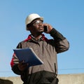 African american builder with work papers talks on smartphone