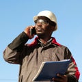 African american builder with work papers talks on smartphone