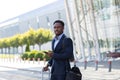 African american business man standing on the background a modern train station airport in formal suit with a suitcase using app