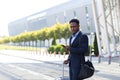 African american business man standing on the background a modern train station airport in formal suit with a suitcase using app