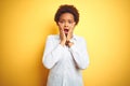 African american business woman over isolated yellow background afraid and shocked, surprise and amazed expression with hands on Royalty Free Stock Photo