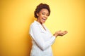 African american business woman over isolated yellow background pointing aside with hands open palms showing copy space, Royalty Free Stock Photo