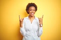 African american business woman over isolated yellow background shouting with crazy expression doing rock symbol with hands up Royalty Free Stock Photo