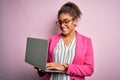 African american business woman wearing glasses working using laptop over pink background with a happy face standing and smiling Royalty Free Stock Photo