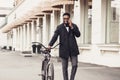 African-american businessman with bike walking and talking on cellphone