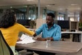 African american businessman doing hands shake with biracial businesswoman sitting at desk Royalty Free Stock Photo