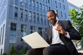 African american businessman outside office building talking to colleagues remotely, boss in business suit with laptop Royalty Free Stock Photo