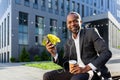 African American businessman sitting outside on a bench headphones, holding a phone, a cup of coffee Royalty Free Stock Photo