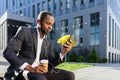 African American businessman sitting outside in headphones, holding a phone, a cup of coffee Royalty Free Stock Photo